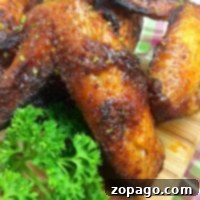 Close-up of seasoned, roasted chicken wings on a wooden cutting board, garnished with fresh parsley. These air fryer wings boast crispy perfection. In the background, part of a plaid cloth is visible.