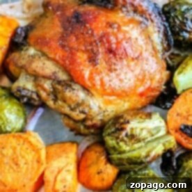 One-Pan Golden Chicken Thighs 5 Sheet pan chicken thighs with charred skin, nestled among baked sweet potatoes, Brussels sprouts, and red onion on a baking sheet.