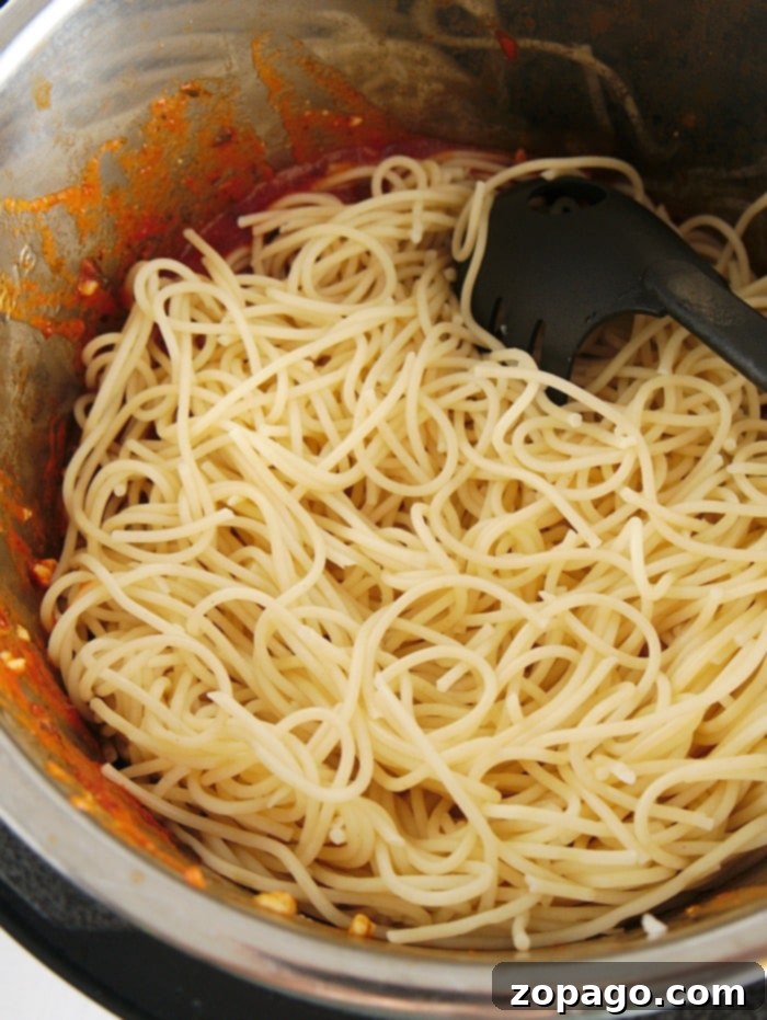 Instant Pot chicken parmesa is here! #instantpot #instantpotrecipes #instantpotchickenparmesan #chickenparmesan #chicken #instantpotchicken #thetypicalmom Spaghetti in a pot with tomato sauce remnants and a black pasta serving spoon, reminiscent of a quick instant pot chicken parmesan evening delight.