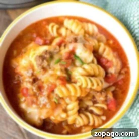 One-Pot Instant Pot Enchilada Casserole 6 A bowl of rotini pasta with savory meat sauce and melted cheese sits enticingly on a wooden surface next to a green cloth, evoking the comforting flavors of an instant pot enchilada casserole.