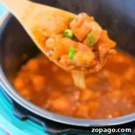A spoonful of spicy chicken stew with green onions above a blue pot, perfect for warming up with one of those hearty January instant pot recipes.