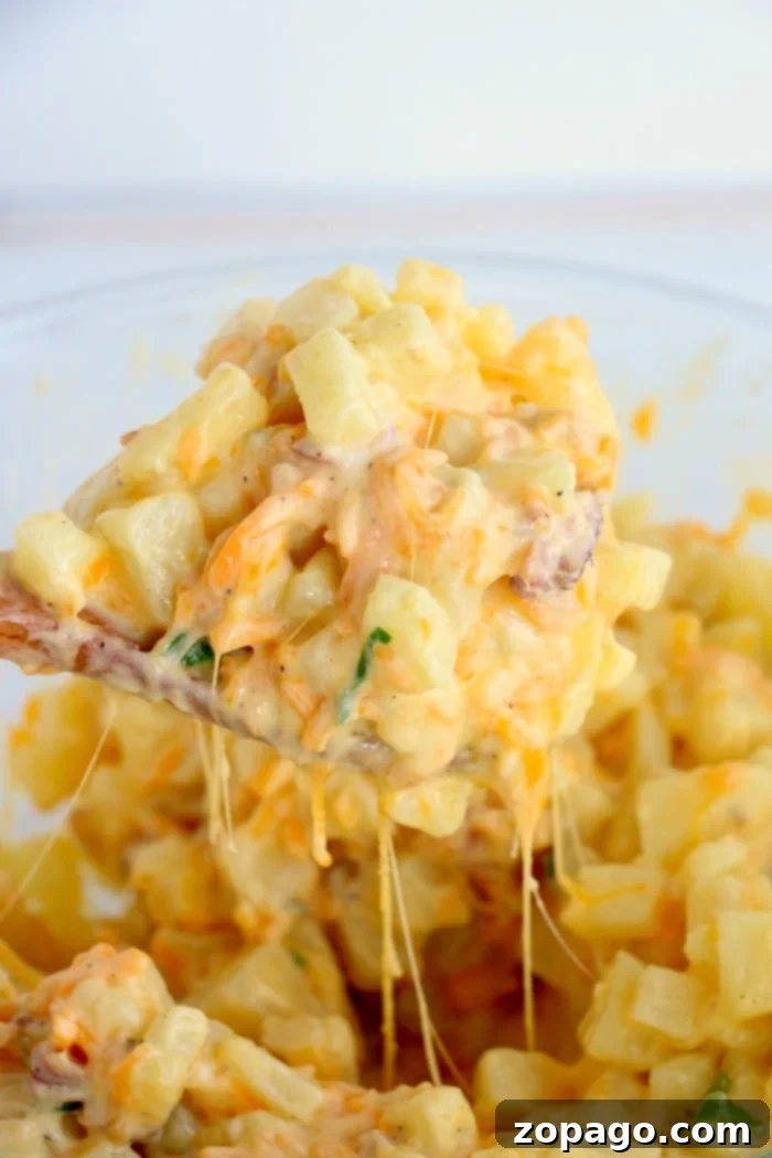 Creamy Cheesy Potato Bake 7 Close-up of a generous spoonful of cheesy potato casserole, with visible strands of melted cheese stretching, crispy bacon pieces, and green herbs, highlighting its rich, creamy texture.