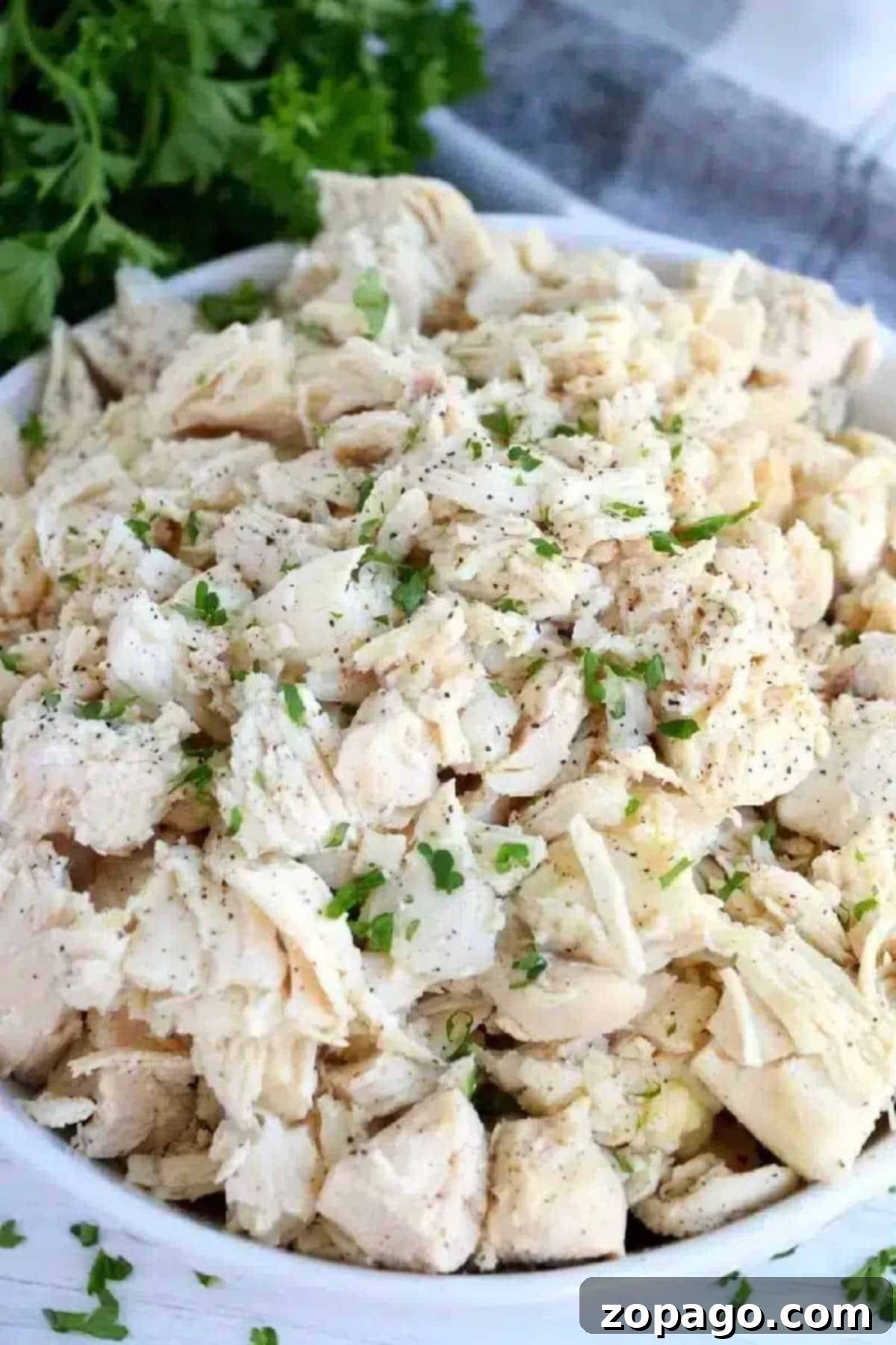 How to Poach Chicken Breast for Tender Shredded Chicken 2 A bowl of shredded cooked chicken, garnished with chopped parsley and black pepper—perfect for anyone learning how to make shredded chicken on the stove.