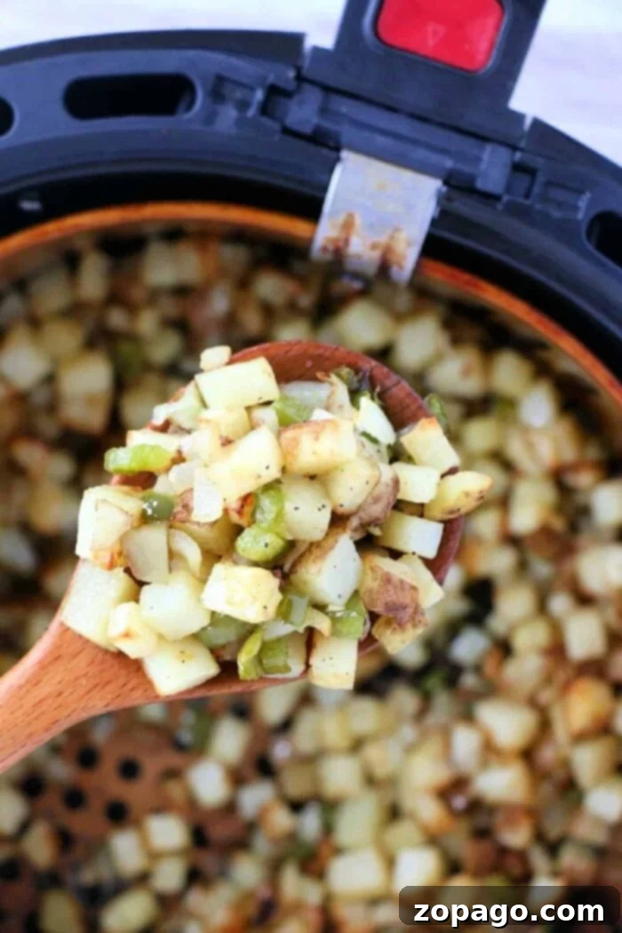Golden Air Fryer Breakfast Spuds 2 A wooden spoon holds diced potatoes and vegetables over an air fryer basket filled with crispy air fryer breakfast potatoes.
