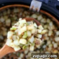 A wooden spoon holds perfectly cooked air fryer breakfast potatoes mixed with vibrant green peppers above the basket.