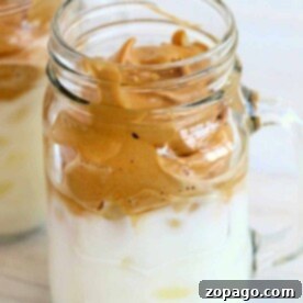 A creamy dalgona whipped coffee delight, elegantly served in a mason jar with its signature frothy crown gracefully resting atop chilled milk.