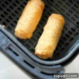 Two frozen egg rolls crisp up perfectly in an air fryer basket, turning golden and delicious.