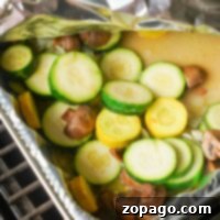 Smoked vegetables take center stage as grilled zucchini and mushrooms are nestled in a foil tray, partially covered with aluminum foil.