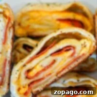 Pizza Swirls 8 Close-up of sliced stromboli with layers of cheese and pepperoni, showcasing a tantalizing twist reminiscent of a Traeger pizza, all beautifully arranged on a white plate.