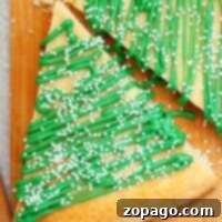 Triangle-shaped christmas tree sugar cookies with green icing and white sprinkles rest elegantly on a wooden board.