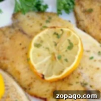 Frozen fish in an air fryer, no breading, are elegantly garnished with a lemon slice and parsley on a white plate.