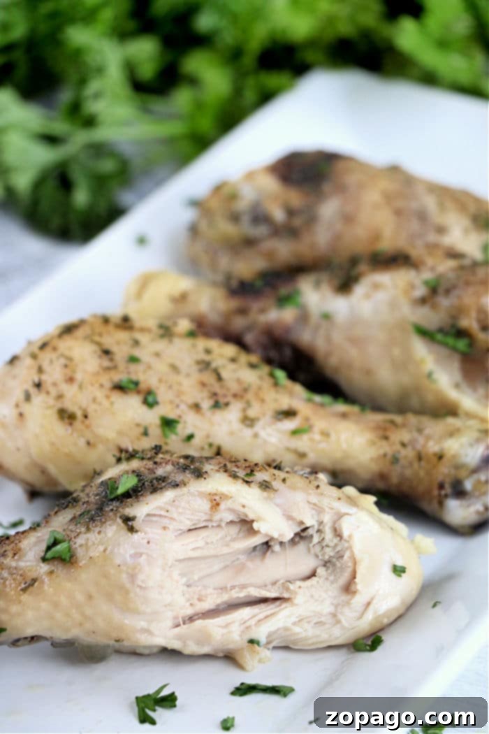 Fall-Off-The-Bone Slow Cooker Chicken Legs 7 Slow-cooked chicken legs rest on a white plate, garnished with fresh herbs, ready to be served.