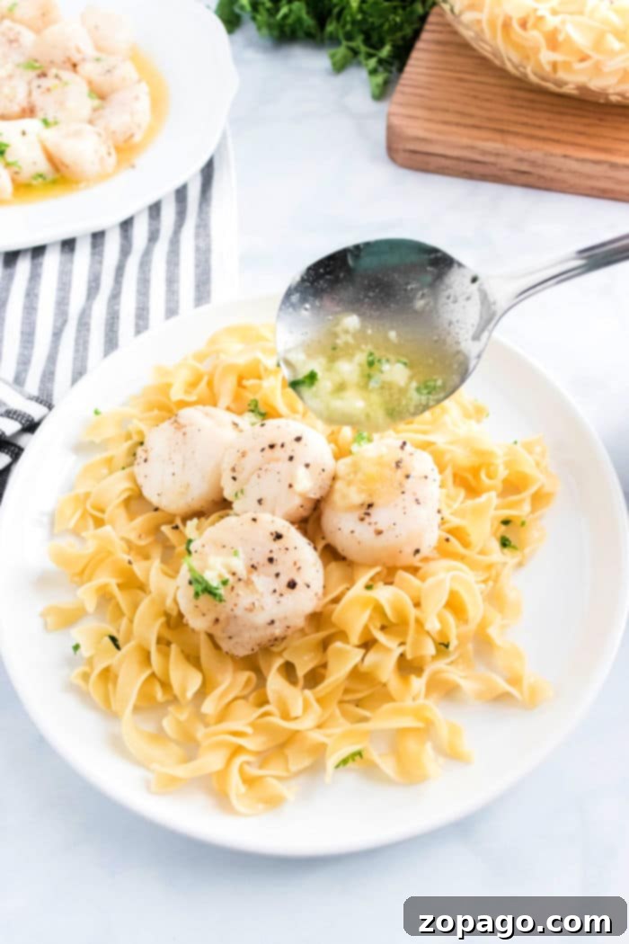 Golden Air Fryer Scallops 2 Plate of pasta topped with perfectly seared air fryer scallops and savory sauce, served with a spoon and striped napkin.