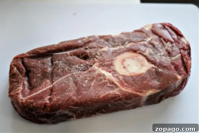 Perfect Beef Arm Roast 4 A raw cut of beef arm roast on a white surface, featuring a bone in the center. The meat has a marbled texture and a reddish-brown color, perfect for your next savory recipe.