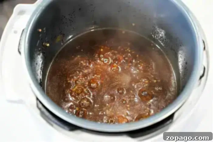 Perfect Beef Arm Roast 8 A close-up of a steaming pot in instant pot reveals a dark, bubbling gravy brimming with spices. The well-worn pot cradles a savory beef arm roast recipe, its contents simmering energetically.