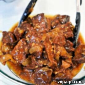 Chunks of braised beef, prepared using a classic beef arm roast recipe, in a rich, glossy sauce with onions, served in a glass bowl with tongs.