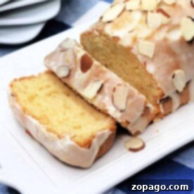 Copycat Starbucks lemon loaf cake with icing and almond slices on a white platter, placed on a blue checkered tablecloth.