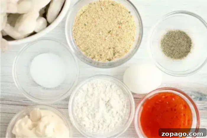Crispy Air-Fried Bang Bang Shrimp 4 Ingredients arranged on a white surface: a small bowl of bread crumbs, black pepper, a white egg, flour, a red sauce for the bang bang shrimp, mayonnaise, salt, and a bowl of raw shrimp ready for the air fryer.