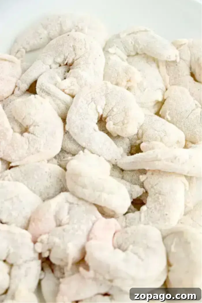 Crispy Air-Fried Bang Bang Shrimp 6 A close-up view of a pile of raw shrimp covered in a layer of flour or breading on a white background, ready to be transformed into crispy air fryer bang bang shrimp.