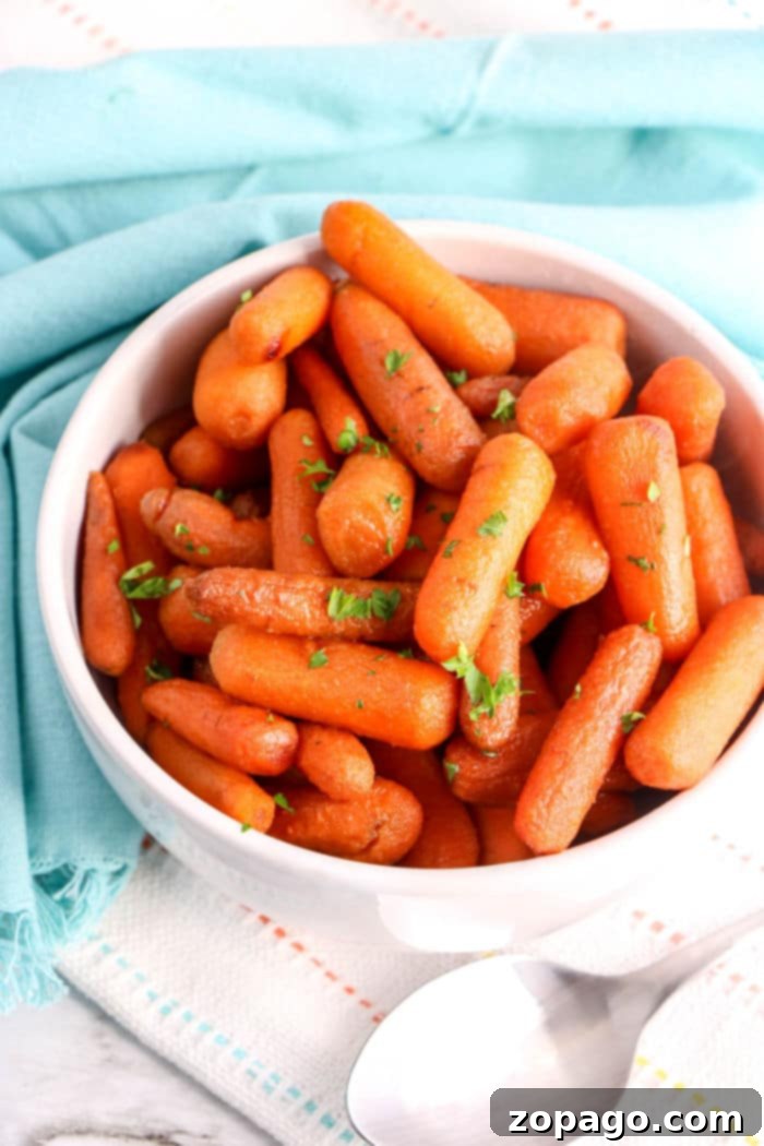 Glazed Slow Cooker Carrots 5 A bowl of tender crockpot carrots garnished with fresh parsley sits on a blue cloth, with a serving spoon nearby.