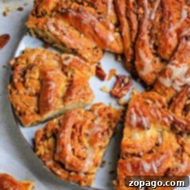 The Art of Braided Bread 11 A spiral pecan cinnamon roll with icing, meticulously crafted like a bread wreath, features enticing slices on a white plate beside a bowl of pecans.