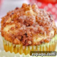 Close-up of an apple zucchini muffin topped with crumbly cinnamon sugar and nuts, nestled in a yellow paper liner.