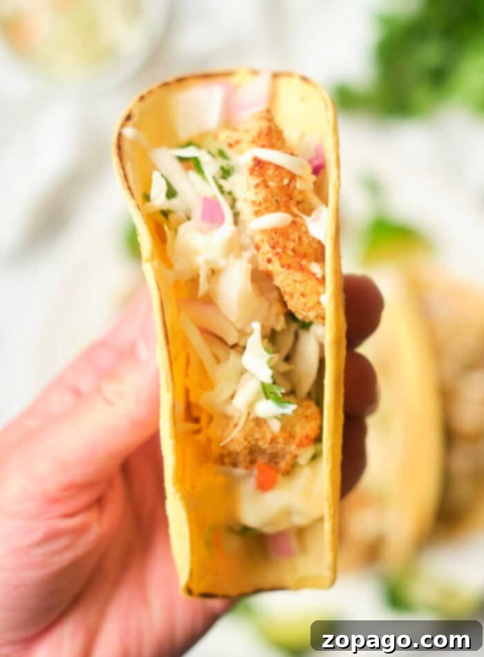 Crispy Air Fryer Fish Tacos 2 A hand holds a taco filled with crispy air fryer fish, shredded cabbage, red onion, and cilantro.