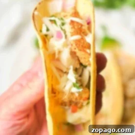 Crispy Air Fryer Fish Tacos 6 A hand holding a taco filled with crispy air fryer fish, coleslaw, and garnished with fresh herbs.