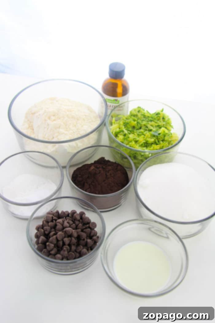 Hidden Veggie Brownies 3 Seven glass bowls hold the ingredients for a zucchini brownie recipe, perfectly arranged on a surface. They include flour, chopped zucchini, sugar, chocolate chips, cocoa powder, a small bowl of liquid, and a bottle of vanilla extract.
