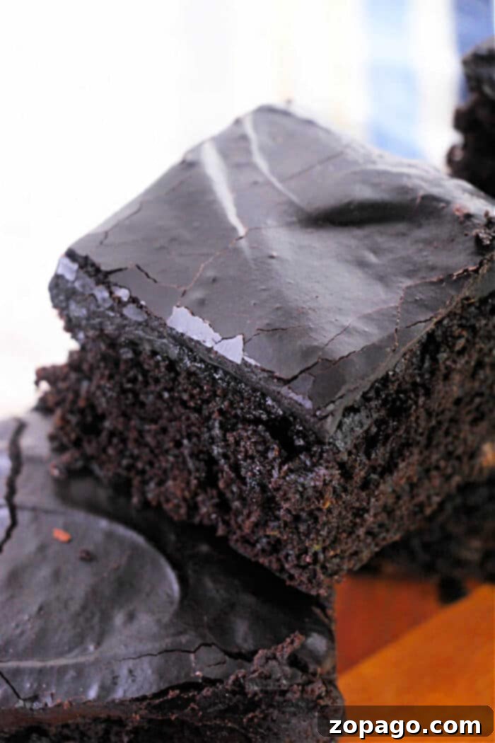 Hidden Veggie Brownies 7 Close-up of a stack of chocolate brownies with a glossy, cracked top layer. Imagining these as part of a zucchini brownie recipe enhances their moist and dense texture, showcasing a rich, dark brown color.