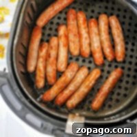 Sausage links in an air fryer basket rest on a sleek black perforated tray.