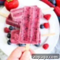Create Perfect Homemade Popsicles 8 A hand holds a berry popsicle, showcasing a vibrant treat among more popsicles and fresh berries on a plate—an enticing glimpse into the delightful world of how to make homemade popsicles.