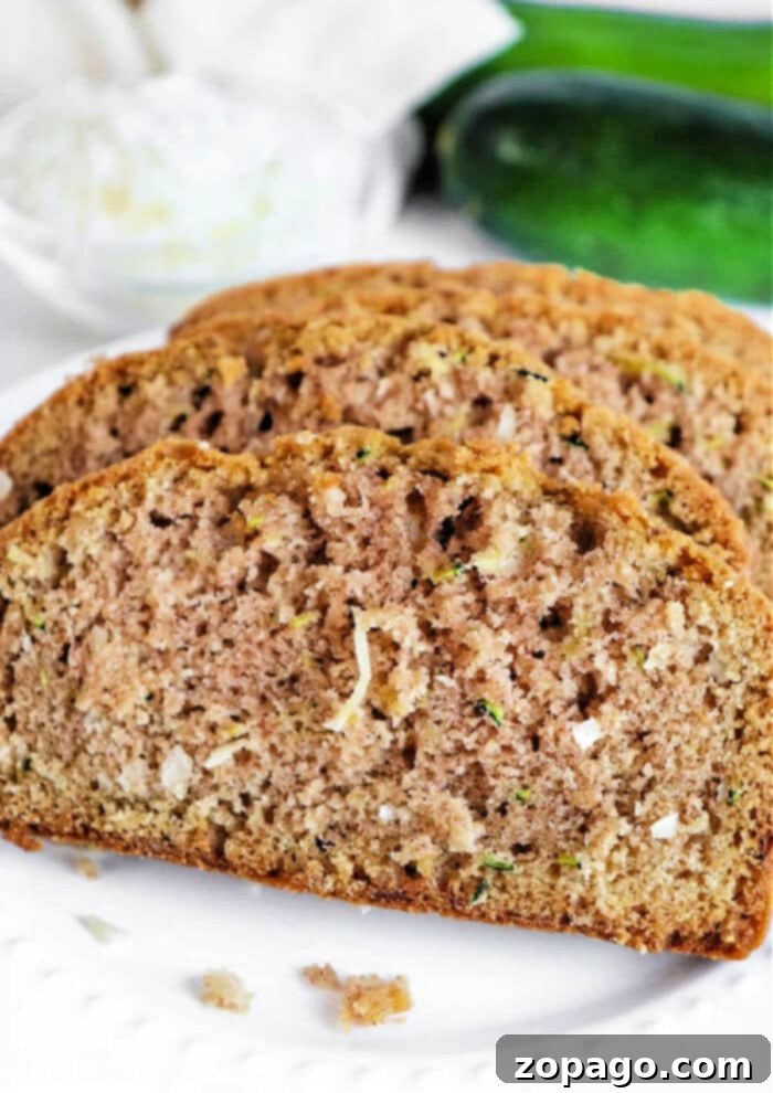 Tropical Zucchini Coconut Loaf 2 Moist Coconut Zucchini Bread slices on a plate with fresh zucchini in the background, highlighting its deliciousness and the hidden vegetable