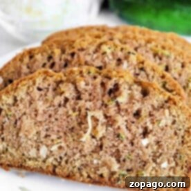 Tropical Zucchini Coconut Loaf 6 Slices of coconut zucchini bread are artfully arranged on a white plate, with a fresh whole zucchini in the background, ready to be enjoyed.
