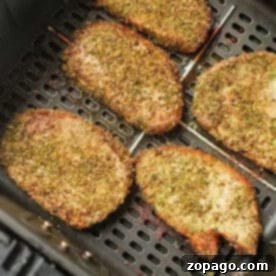 Seasoned pork chops, or pork steak in air fryer, cook to golden brown perfection, evenly spaced in the basket.