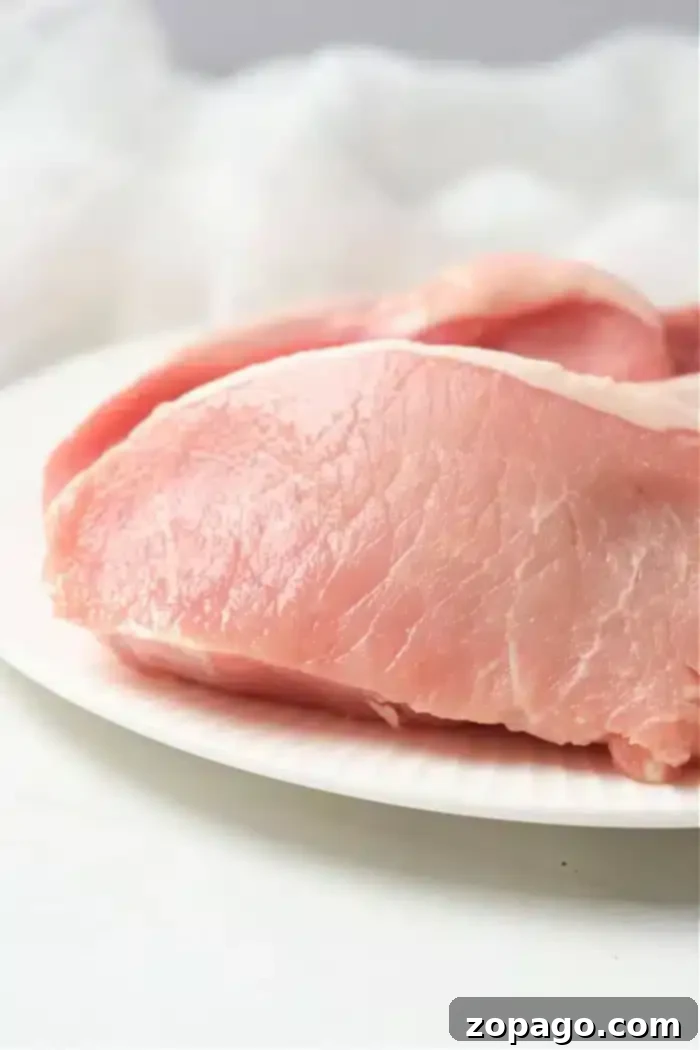 Perfect Air Fryer Pork Steak 9 Close-up of raw, boneless pork chops prepared for an air fryer on a white plate. The fresh, pink meat boasts visible marbling against a softly blurred, white background.