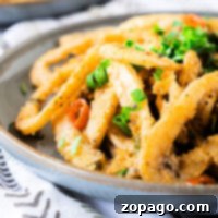 Mastering Crispy Calamari at Home 6 Fried calamari, a testament to mastering how to cook calamari perfectly, is garnished with chopped herbs on a gray plate, set on a patterned cloth.