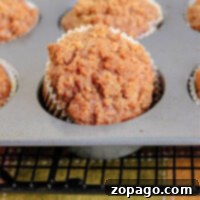 A tray of freshly baked pumpkin streusel muffins with crumbly tops, one muffin raised higher in a paper liner.