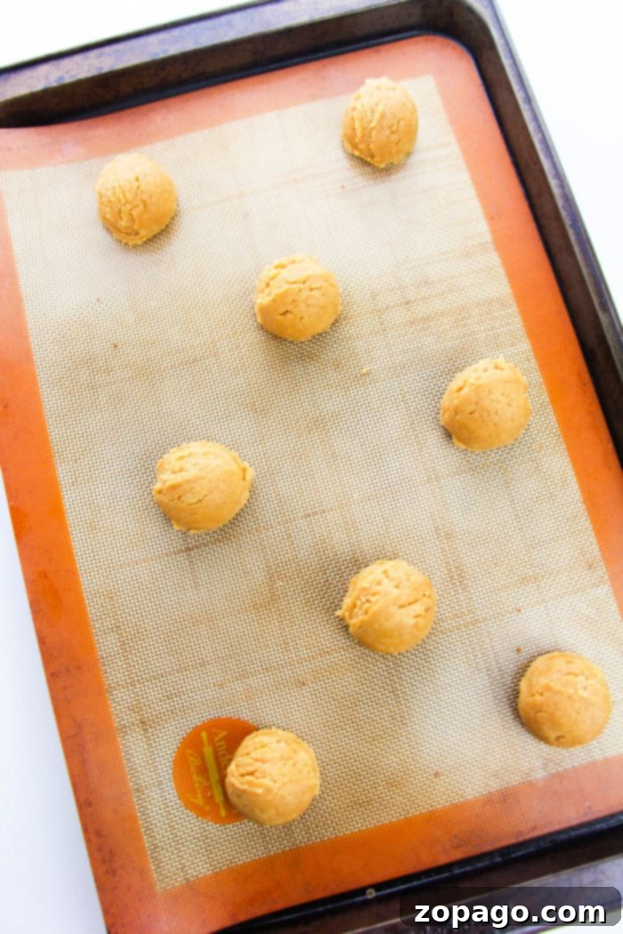 Effortless Four Ingredient Peanut Butter Cookies 4 Eight perfectly portioned peanut butter cookie dough balls, with the classic crisscross fork marks, resting on a baking tray lined with a silicone mat, awaiting baking.