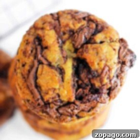 Close-up of a stack of Banana Nutella Muffins with visible chunks of chocolate on a white background, tempting enough to rival the allure of freshly baked Banana Nutella Muffins.