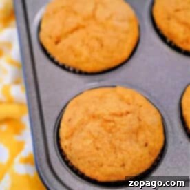 A muffin tin holds six freshly baked golden brown Cake Mix Pumpkin Banana Muffins on a yellow patterned cloth.