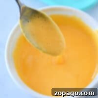 A spoon dipped in a bowl of creamy orange cheese sauce showcases the perfect velveeta blend, demonstrating how to make velveeta cheese sauce effortlessly delicious.