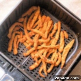 Golden chicken fries in an air fryer basket rest on a beige surface, promising a crispy delight.
