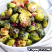 A white bowl filled with roasted Brussels sprouts and cranberries drizzled in a rich balsamic glaze rests on a woven placemat.