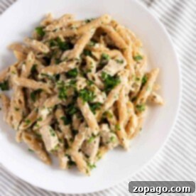 A plate of creamy Slow Cooker Chicken Alfredo, made with tender frozen chicken and fresh herbs, rests invitingly on a striped tablecloth.