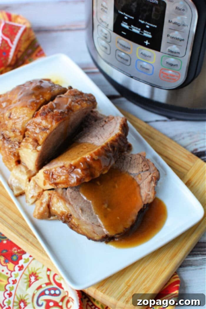 Tender Instant Pot Rump Roast 2 Sliced roast beef with gravy, made from a tender instant pot rump roast, served on a white plate next to an Instant Pot on a wooden board.