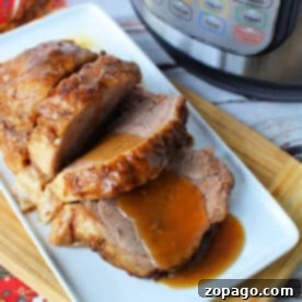 Sliced roast beef with gravy, made from a tender instant pot rump roast, served on a white plate next to an Instant Pot on a wooden board.
