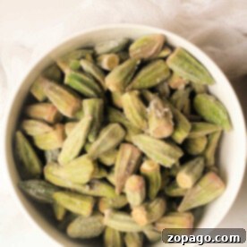 A bowl of frozen okra pieces sits on a light surface with a white cloth nearby, ready for their transformation in the air fryer.