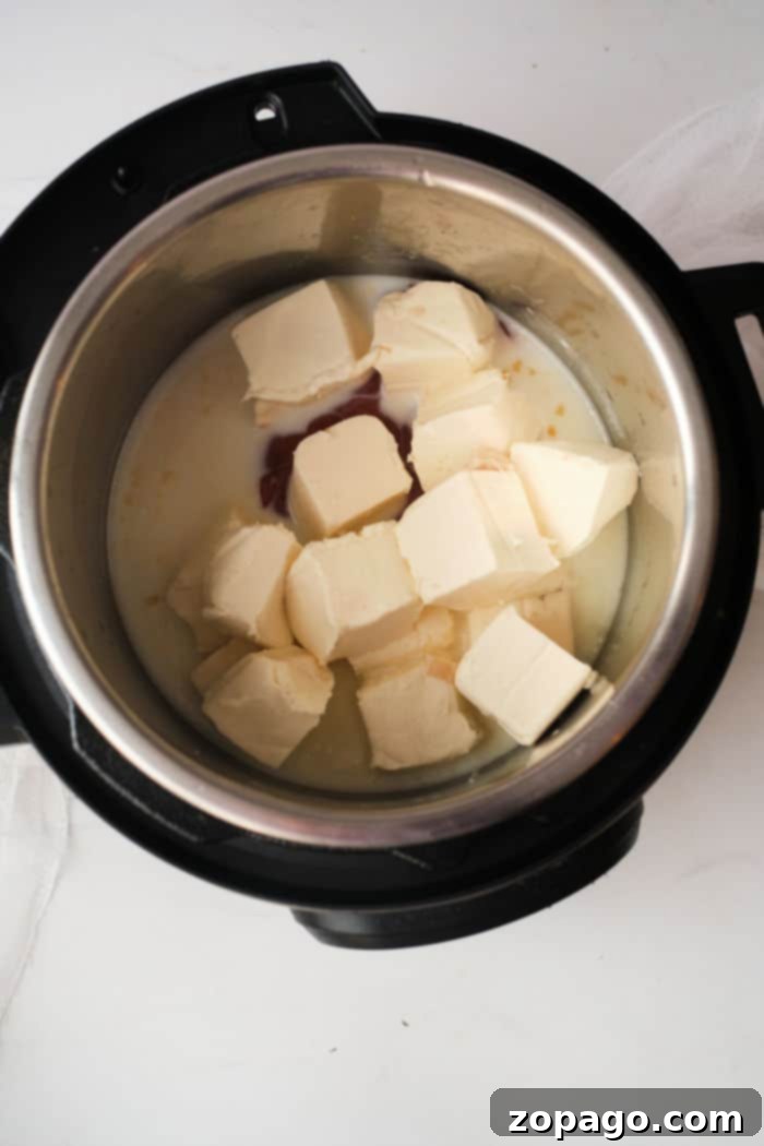 Instant Pot Buffalo Chicken Dip 5 Cubes of cream cheese in a metal pot, partially melted alongside a creamy buffalo chicken dip liquid.