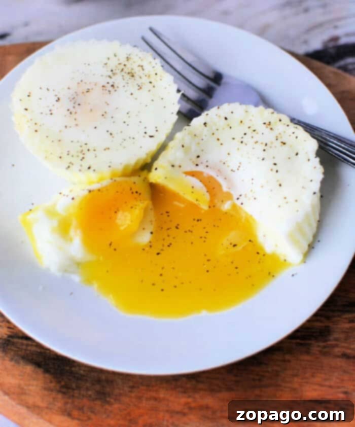 Effortless Slow Cooker Eggs 2 Two poached eggs on a white plate, with one cut open to reveal runny yolk spilling out, sprinkled with black pepper. Perfectly tender like slow cooker eggs, a fork rests beside them.